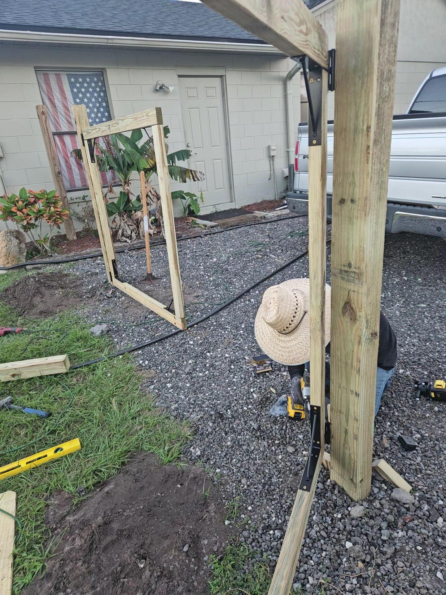 Person building a wooden frame structure in a yard with construction tools and materials around.