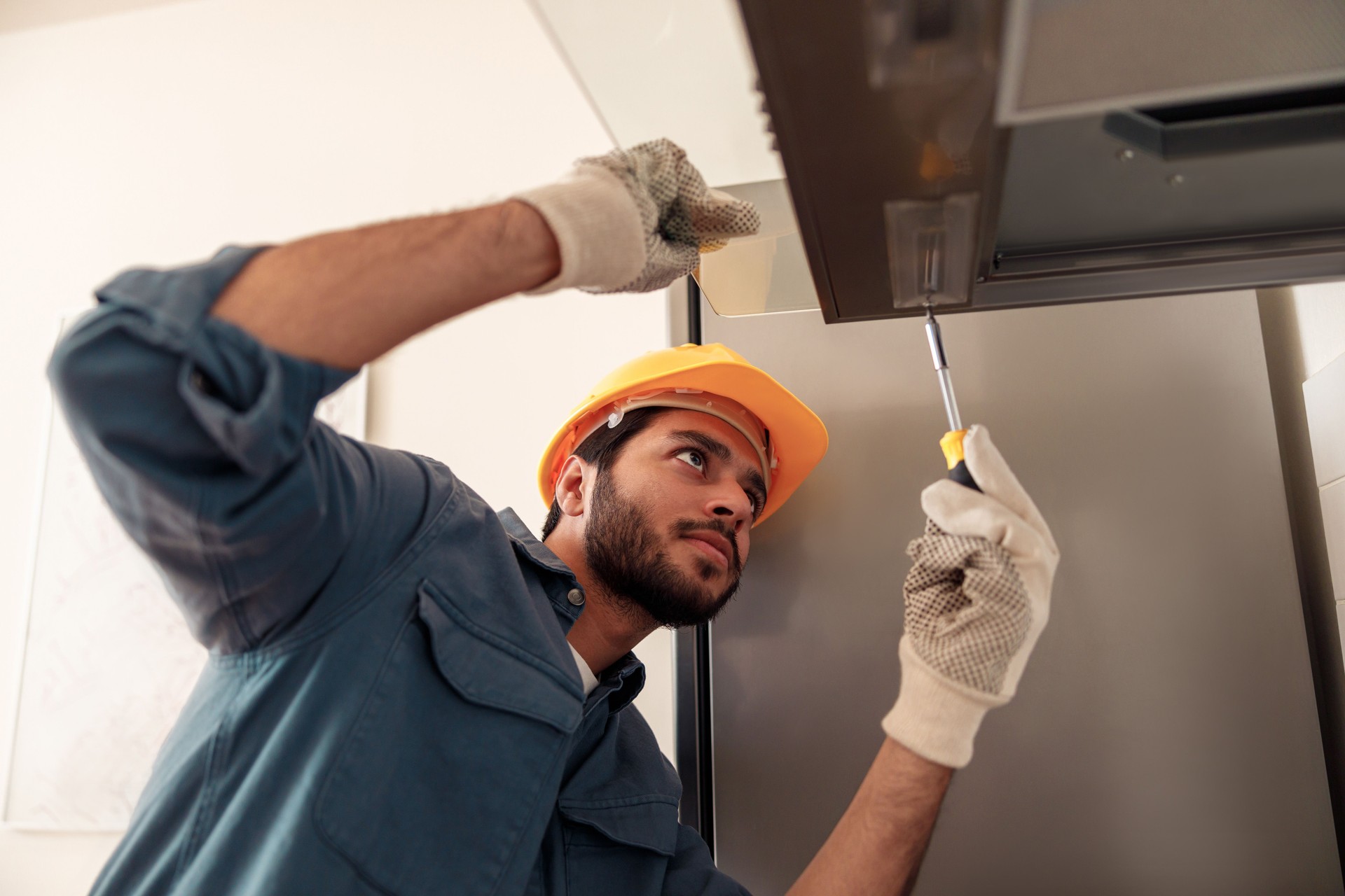 Handyman in uniform repairing kitchen extractor, replacing filter in cooker hood.Maintenance concept